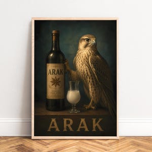 May include: A framed wall art print featuring a brown falcon standing next to a dark glass bottle labeled ARAK with a star icon and a small glass filled with a milky white liquid. The word ARAK is printed in large capital letters at the bottom.