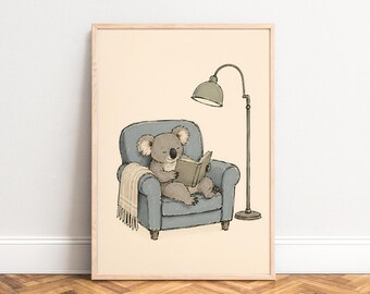 May include: A framed illustration featuring a grey koala sitting in a blue armchair, reading an open book. A beige fringed blanket is draped over the arm of the chair, and a tall, slender floor lamp with a green shade stands beside the armchair.