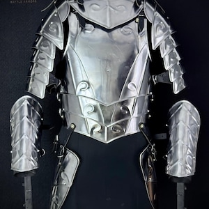Op de afbeelding: Een gepolijste stalen gevechtsrusting, inclusief borstplaat, schouderbeschermers en armbeschermers. De bepantsering heeft decoratieve krullen en wordt getoond op een zwarte mannequin. Het Steel Heritage-logo is linksboven zichtbaar.