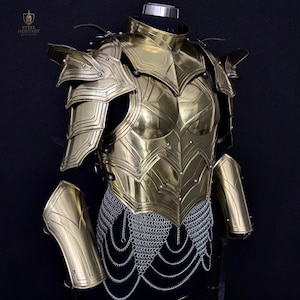 May include: A golden-colored breastplate and shoulder armor set, displayed on a mannequin. The armor features intricate layered designs, rivets, and a chainmail skirt. The Steel Heritage logo is visible in the upper left corner. The set includes arm guards.