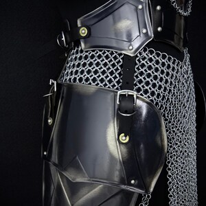 May include: Close-up of medieval armor, featuring a combination of polished metal plates and chainmail. The armor includes a breastplate, shoulder guards, and leg protection, all secured with leather straps and buckles. The Steel Heritage logo is visible.