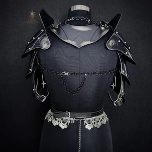 May include: Black leather armor set displayed on a mannequin. The set includes shoulder pauldrons, a gorget, and a belt with decorative silver accents. A chain with cross pendants hangs from the armor. The Steel Heritage logo is visible in the upper left corner.
