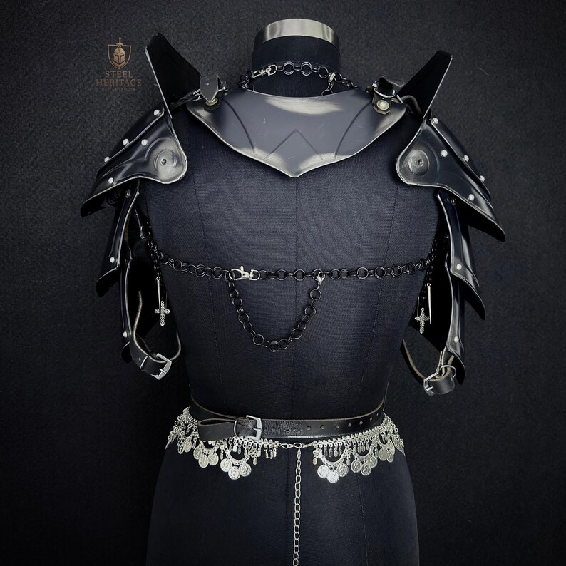 May include: Black leather armor set displayed on a mannequin. The set includes shoulder pauldrons, a gorget, and a belt with decorative silver accents. A chain with cross pendants hangs from the armor. The Steel Heritage logo is visible in the upper left corner.