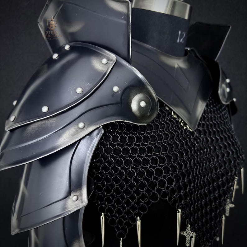 May include: Close-up of a black steel shoulder armor set with riveted accents and a chainmail underlayer. The armor is displayed on a mannequin, showcasing its design and construction. The Steel Heritage logo is visible.