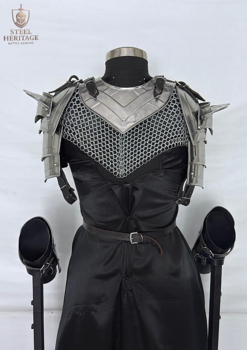 May include: A medieval-style steel armor set, including a chest plate, shoulder guards, and chainmail, displayed on a mannequin. The armor is silver-colored and features pointed shoulder spikes. The mannequin is dressed in a black outfit with a leather belt.