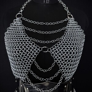 May include: A silver chainmail top with a halter neckline and layered chain details. The armor is displayed on a black mannequin, with a black leather belt at the waist. The Steel Heritage Battle Armors logo is visible in the upper left corner.