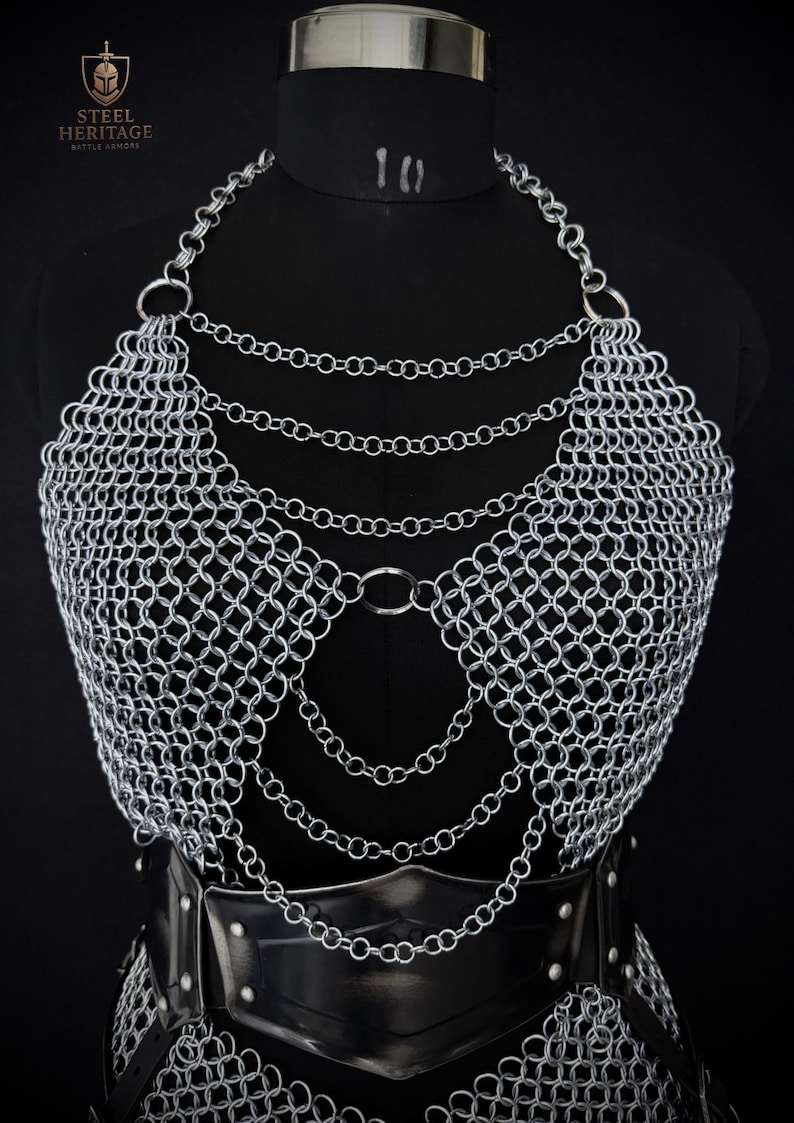 May include: A silver chainmail top with a halter neckline and layered chain details. The armor is displayed on a black mannequin, with a black leather belt at the waist. The Steel Heritage Battle Armors logo is visible in the upper left corner.