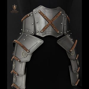 May include: A steel waist armour piece featuring a central plate with a copper-coloured chain cross design, layered side tassets, and decorative circular metal accents. The piece includes the Steel Heritage logo text in the upper left corner.