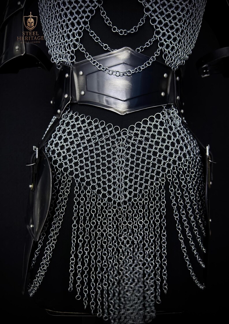 May include: Close-up of a medieval chainmail armor set. The armor features a silver chainmail design with a black leather belt and accents. The Steel Heritage logo is visible in the upper left corner. The armor is designed to protect the torso.