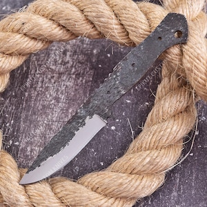 May include: A fixed-blade knife blank featuring a dark, textured, forged-style finish on the spine and handle area, transitioning to a smooth, polished, silver-colored metal blade edge. The text EPIKUT KNIVES is visible on the blade surface.