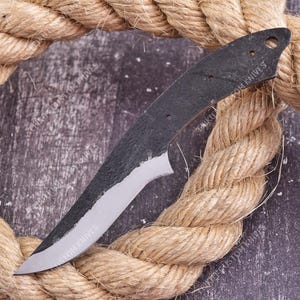 May include: A metal knife blade blank with a dark, textured finish on the upper portion and a polished, silver-colored edge. The handle section features three small circular holes. The text EPIKOT CUSTOM KNIVES is visible on the blade surface.
