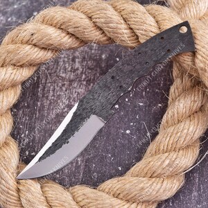 May include: A knife blade with a dark, textured finish on the upper portion and a smooth, polished silver edge. The handle area features a series of small circular holes for mounting. The text EPIKUT CUSTOM KNIVES is visible on the blade.