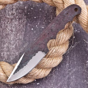 May include: A metal knife blade blank with a dark, textured, forged finish on the upper portion and a polished, sharpened edge. The handle section features a circular hole for mounting. The text EPIKUT CUSTOM KNIVES is visible on the blade.
