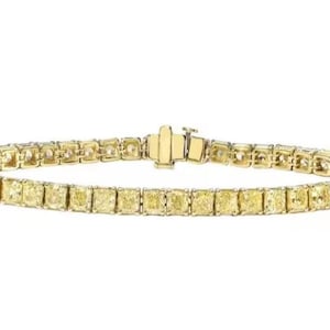 Könnte beinhalten: Ein goldenes Armband mit einer Reihe gelber, rechteckiger Edelsteine. Das Armband wird mit einem Verschluss gesichert. Die Edelsteine sind eng aneinander gesetzt und bilden eine durchgehende Farblinie. Das Armband wird vor weißem Hintergrund gezeigt.