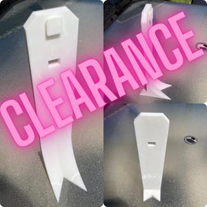 May include: A white vertical display stand with a tapered top and a bifurcated base, featuring a small rectangular cutout and a raised square detail on the front surface. The word CLEARANCE is overlaid in large pink text across the image.