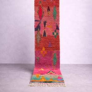 May include: A vibrant, rectangular rug with a textured, woven design. The rug features a color palette of pink, orange, green, and yellow geometric shapes. The rug has a fringed edge and is displayed against a neutral background.