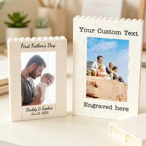 Könnte beinhalten: Zwei cremefarbene Bilderrahmen aus Steckbausteinen. Ein Rahmen zeigt ein Foto mit dem Text "First Father's Day" und "Daddy & Sophia June 15 2025". Der andere Rahmen hat den Text "Your Custom Text" und "Engraved here".