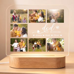 Könnte beinhalten: Eine personalisierte Fotodisplay-Lampe zum Vatertag. Die Lampe hat einen Holzsockel und eine transparente Acrylplatte mit Familienfotos. Die Worte "Papa, wir lieben dich" sind auf die Platte gedruckt. Ein Banner mit der Aufschrift "Happy Father's Day" hängt im Hintergrund.