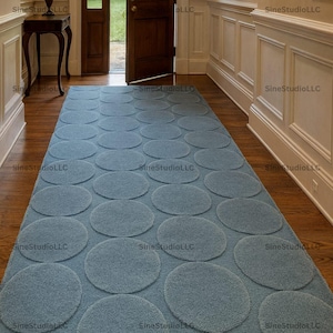 Könnte beinhalten: Ein rechteckiger, hellblauer Teppich mit einem Muster aus großen, gleichmäßig verteilten Kreisen. Der Teppich liegt auf einem Holzboden in einem Flur, mit einer dunklen Holztür und Verkleidung im Hintergrund. Das Design des Teppichs verleiht dem Raum eine moderne Note.
