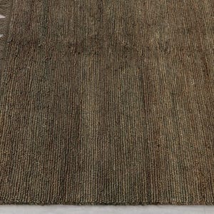 May include: Close-up of a brown woven rug with a fringed edge. The rug has a textured surface with vertical lines and varying shades of brown. The rug is made of natural fibres.