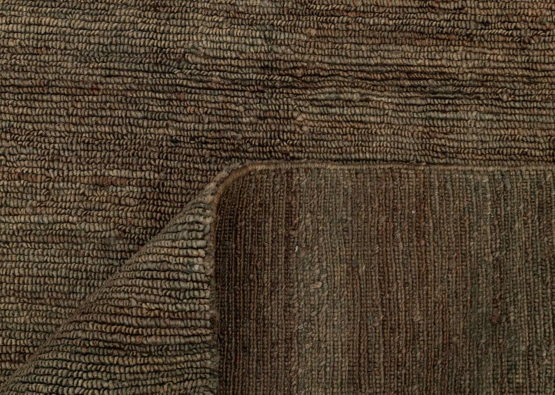 May include: Close-up of a brown woven rug with a textured surface. The rug is folded over, revealing the underside with a different weave pattern. The colour is a dark, earthy brown.