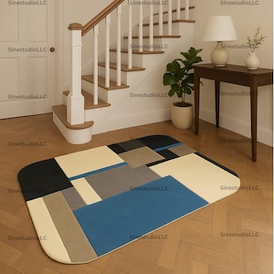 May include: A rectangular area rug with a geometric pattern in shades of blue, beige, gray, and black. The rug has rounded corners and is placed on a hardwood floor. The image also shows a staircase, a table with a lamp, and a potted plant.