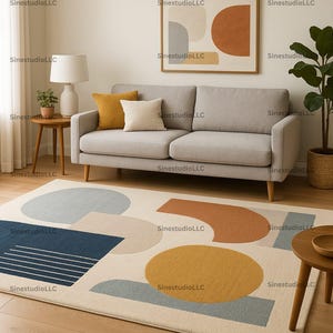 Könnte beinhalten: Ein modernes Wohnzimmer mit einem hellgrauen Sofa mit Holzbeinen, verziert mit senf- und cremefarbenen Kissen. Ein geometrischer Teppich mit blauen, senf- und beigefarbenen Formen liegt auf dem Holzboden. Ein gerahmtes abstraktes Kunstwerk hängt über dem Sofa.