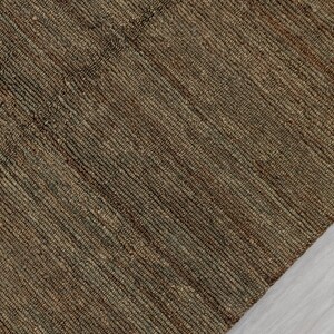 May include: A close-up of a woven rug with a textured surface. The rug is primarily brown with subtle variations in colour, creating a natural, earthy appearance. The weave pattern is visible, adding to the rug's rustic charm. The rug is made of natural fibres.