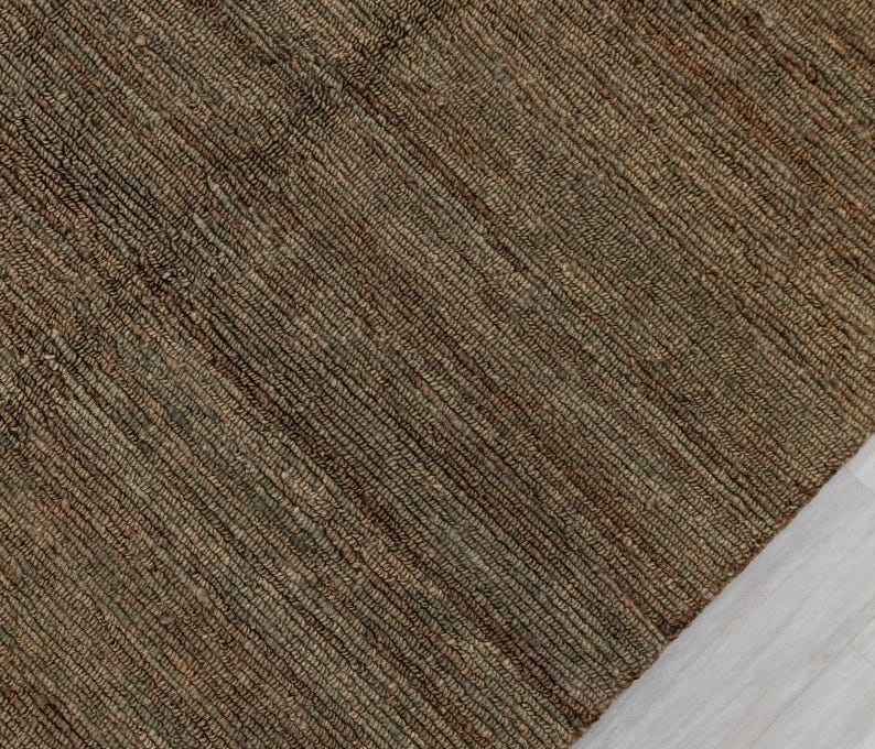 May include: A close-up of a woven rug with a textured surface. The rug is primarily brown with subtle variations in colour, creating a natural, earthy appearance. The weave pattern is visible, adding to the rug's rustic charm. The rug is made of natural fibres.