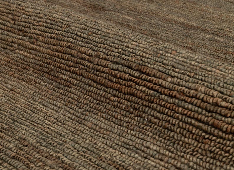 May include: Close-up of a textured, woven rug. The rug features a natural colour palette with shades of brown and tan. The fibres are tightly woven, creating a durable and visually appealing surface. The rug's texture adds warmth and a rustic feel to any space.