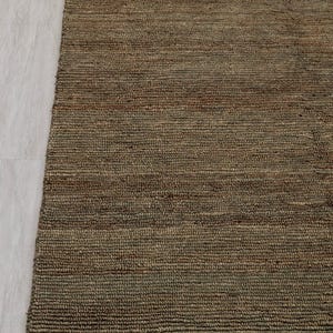 May include: A brown woven rug with a textured surface and fringed edge. The rug is made from natural fibres and has a neutral colour, suitable for various interior styles. The rug's dimensions are in centimetres.