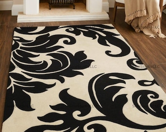 May include: A rectangular area rug with a cream background and a large black floral pattern. The rug is placed in front of a fireplace with a burning fire. A white chair with a tan throw is to the right.