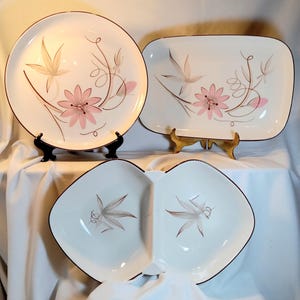 May include: A set of vintage white ceramic serving dishes with a floral design. The set includes a round plate, a rectangular platter, and a divided dish. Each piece features pink flowers, brown stems, and a brown rim.