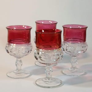 May include: A set of four stemmed glasses featuring a deep red upper bowl and a clear, textured glass base with a repeating circular pattern. Each glass has a flared rim, a short decorative stem, and a circular foot, creating a uniform appearance.