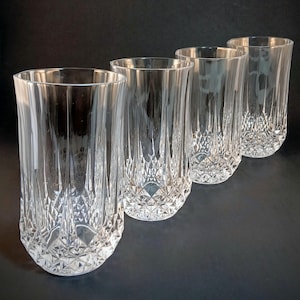 May include: A set of four clear glass tumblers featuring a vertical fluted design on the upper portion and a textured diamond-cut pattern around the base. Each cylindrical drinking glass has a smooth rim and a heavy, faceted bottom.