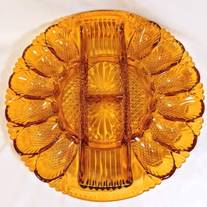 May include: A round amber-colored glass serving platter featuring a central rectangular divider and twelve individual shell-shaped compartments arranged around the perimeter. The glass surface displays a textured diamond pattern and scalloped edges.