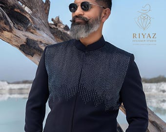 Puede incluir: Chaqueta de traje azul marino oscuro con cuello mao y costuras plateadas decorativas en el pecho. La chaqueta tiene dos bolsillos delanteros y se combina con un pantalón a juego. El texto "RIYAZ DESIGNER STUDIO" está incluido.