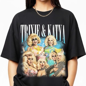 May include: Black t-shirt featuring a group of drag queens with the text "Trixie & Katya" in a stylized font. The graphic includes images of the queens with blonde wigs and colorful outfits, set against a blue and white background.