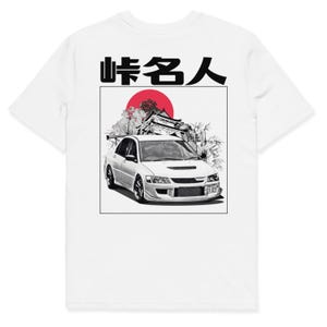 May include: White t-shirt featuring a graphic of a white sports car with a red sun, Japanese text, and a black rectangular border. The car has a spoiler and is set against a backdrop of a mountain and bamboo.