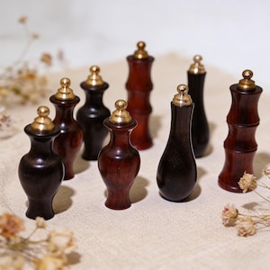 May include: A collection of small, decorative wooden bottles with brass-colored tops. The bottles vary in shape and shade, ranging from dark brown to reddish-brown. Some have a bamboo-like design, while others are more traditionally shaped.