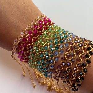May include: A selection of beaded bracelets in a range of colours, including pink, red, green, blue, purple, and black. Each bracelet features small, colourful beads strung together with gold-coloured metal beads. The bracelets are displayed on a wrist.