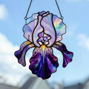 May include: Stained glass iris flower suncatcher with a black metal frame. The flower features shades of purple, blue, and yellow, with a detailed design. The suncatcher hangs from a black chain, perfect for window or wall decor.