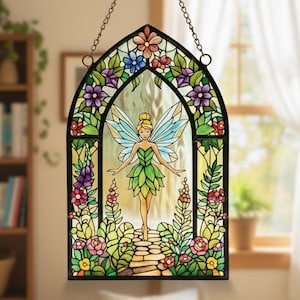 Könnte beinhalten: Buntglas-Fensterbild mit einer Fee in einem grünen Blätterkleid mit blauen Flügeln, umgeben von bunten Blumen und Blättern. Das Panel ist schwarz gerahmt und hängt an einer Kette, wodurch ein skurriles und dekoratives Stück entsteht.