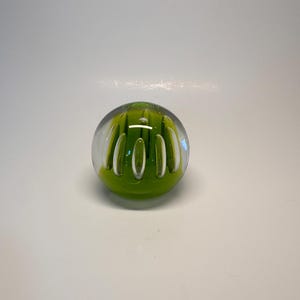 Peut inclure: Presse-papier sphérique en verre transparent. L'intérieur est vert vif avec des accents blancs verticaux. Le verre transparent révèle le motif vert et blanc. Objet décoratif pour bureau ou table.