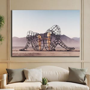 May include: A large framed artwork depicts two wireframe human figures in a seated embrace against a desert landscape. The room features a cream-colored sofa, wooden furniture, and a neutral color palette.