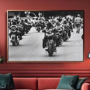 May include: A monochrome framed print of a motorcycle club on a road hangs above a red sofa with teal cushions. The room features red walls, a large plant, and a modern floor lamp.