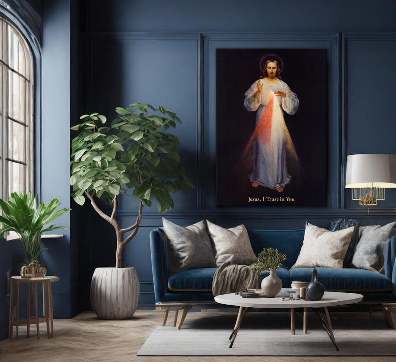 May include: A living room with a blue sofa, a round coffee table, and a large framed artwork depicting a religious figure. A potted tree and a small side table with a plant are also present. The artwork has the text "Jesus, I Trust in You".