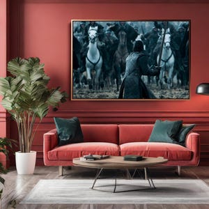 May include: A living room with a red sofa, green pillows, and a wooden coffee table. A large framed artwork depicting a battle scene with horses and figures hangs above the sofa. A tall plant in a white pot and a black floor lamp are also present.