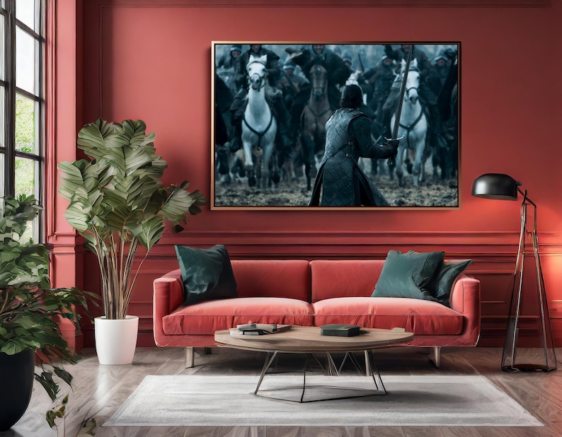 May include: A living room with a red sofa, green pillows, and a wooden coffee table. A large framed artwork depicting a battle scene with horses and figures hangs above the sofa. A tall plant in a white pot and a black floor lamp are also present.