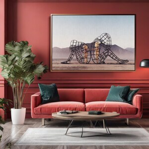May include: A living room with a red sofa, teal pillows, and a wooden coffee table. A large framed artwork depicts wireframe figures on a desert landscape. A tall plant in a white pot and a black floor lamp complete the decor.